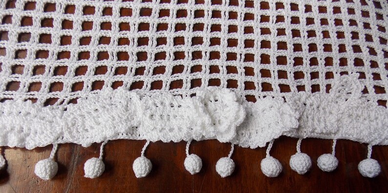 May include: White crocheted table runner with a scalloped edge and white pom-pom trim.