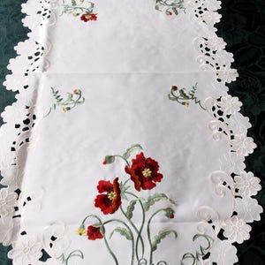 Può includere: Tovaglia da tavolo bianca con un delicato bordo in pizzo e papaveri rossi ricamati. La tovaglia è realizzata in un tessuto fine e ha un design classico.