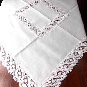 Peut inclure: Nappe blanche avec une bordure en dentelle délicate. La dentelle présente un motif floral avec un bord festonné. La nappe est faite d'un tissu doux et léger.