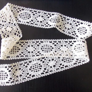 May include: White crochet lace trim with a delicate floral pattern. The lace is approximately 1 inch wide and has a scalloped edge.
