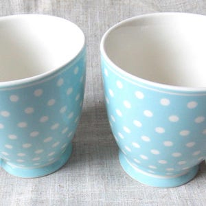 Può includere: Due tazze in ceramica blu con pois bianchi. Le tazze hanno una forma arrotondata e un manico sul lato destro.