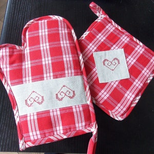 May include: Two red and white checked oven mitts with embroidered hearts. One mitt is a pot holder with a single heart, and the other is a full mitt with two hearts.