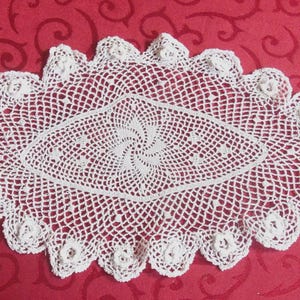 May include: White crocheted oval doily with a delicate floral design. The doily has a center swirl pattern and a scalloped edge.