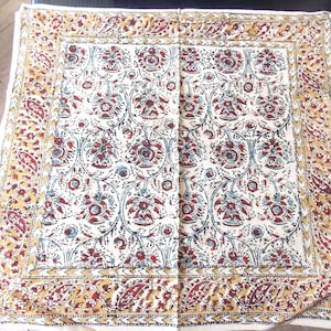 May include: A white cotton square fabric with a repeating floral pattern in shades of red, blue, and brown. The fabric has a gold border with a paisley design.