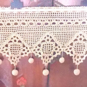 Peut inclure: Une cantonnière en crochet de couleur crème avec un motif géométrique et de petits pompons suspendus. Le design en dentelle complexe présente des formes de diamants et un bord festonné. Ce textile fait main ajoute une touche de charme vintage.