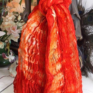 Peut inclure: Une écharpe rouge et orange tie-dye avec une texture plissée. L'écharpe est nouée autour du cou d'un mannequin.