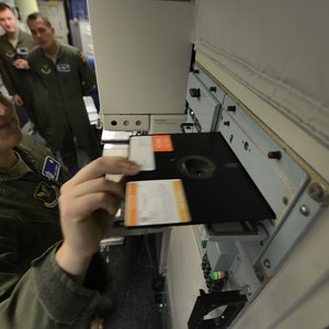 Pode incluir: Uma mulher com uniforme militar verde insere um disquete em uma unidade de disco de computador. A unidade est&aacute; etiquetada como "United States Air Force".