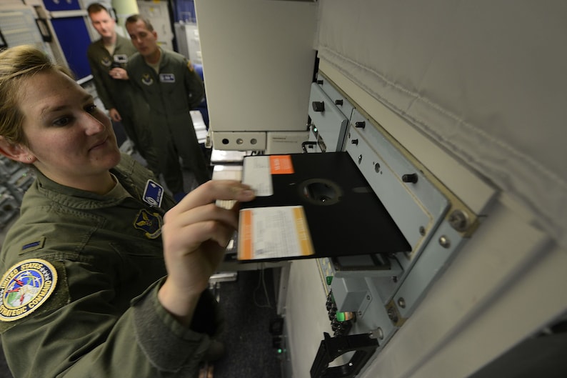 Pode incluir: Uma mulher com uniforme militar verde insere um disquete em uma unidade de disco de computador. A unidade est&aacute; etiquetada como "United States Air Force".