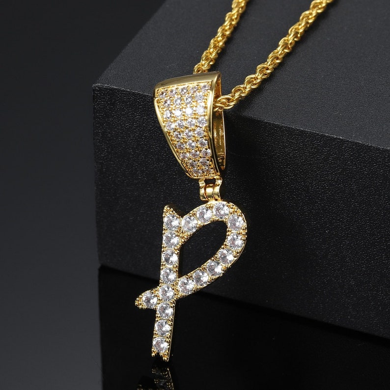 May include: A gold chain necklace with a pendant in the shape of the letter "P". The pendant is encrusted with clear cubic zirconia stones.