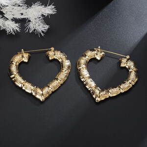 May include: A pair of gold heart-shaped hoop earrings with a bamboo-like texture. The earrings are large and have a hinged closure.