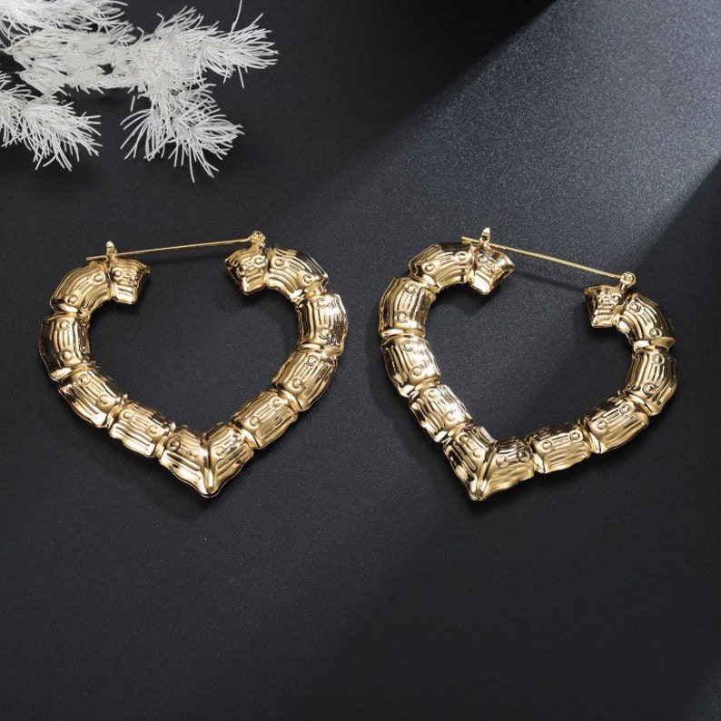 May include: A pair of gold heart-shaped hoop earrings with a bamboo-like texture. The earrings are large and have a hinged closure.