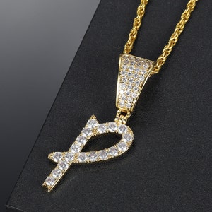 May include: Gold chain necklace with a pendant in the shape of the letter "P" encrusted with clear cubic zirconia stones.