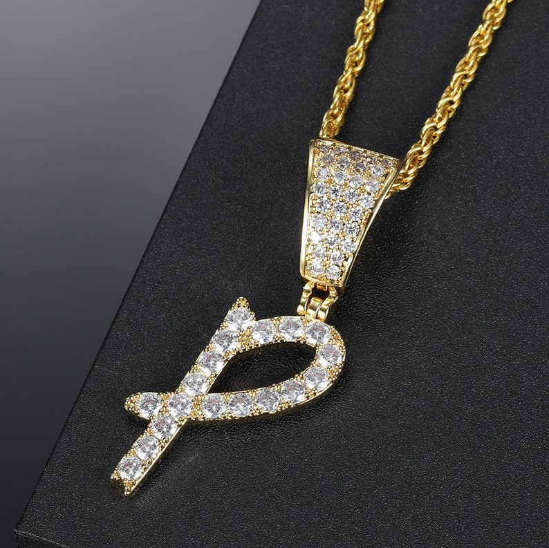 May include: Gold chain necklace with a pendant in the shape of the letter "P" encrusted with clear cubic zirconia stones.