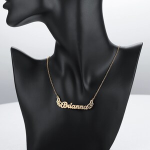 K&ouml;nnte beinhalten: Eine goldene Halskette mit dem Namen "Brianna" in Kursivschrift mit kleinen Fl&uuml;geln auf beiden Seiten des Namens.