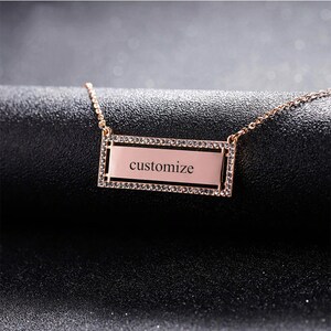 May include: Rose gold necklace with a rectangular pendant. The pendant is inscribed with the word "customize" and is framed with a row of small, clear crystals. The necklace chain is delicate and also rose gold.
