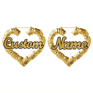 May include: A pair of gold heart-shaped hoop earrings with the words "Custom" and "Name" written in black cursive lettering.