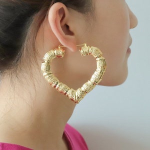 May include: Gold heart-shaped hoop earrings with a bamboo-like texture. The earrings are large and have a thick, substantial design.