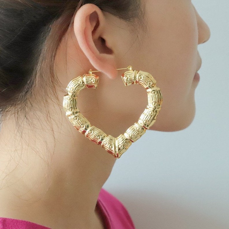 May include: Gold heart-shaped hoop earrings with a bamboo-like texture. The earrings are large and have a thick, substantial design.