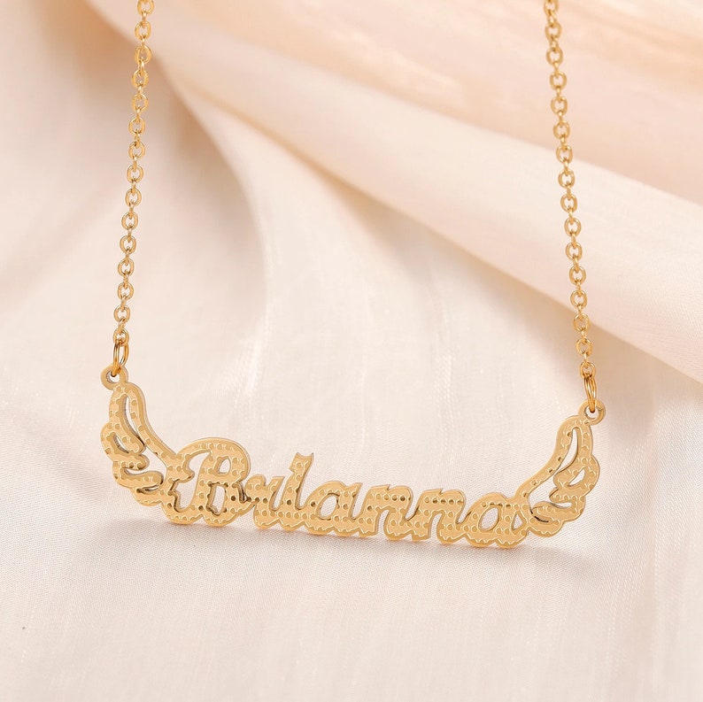 K&ouml;nnte beinhalten: Goldkette mit dem Namen "Julianna" in Kursivschrift mit Fl&uuml;geln auf beiden Seiten.