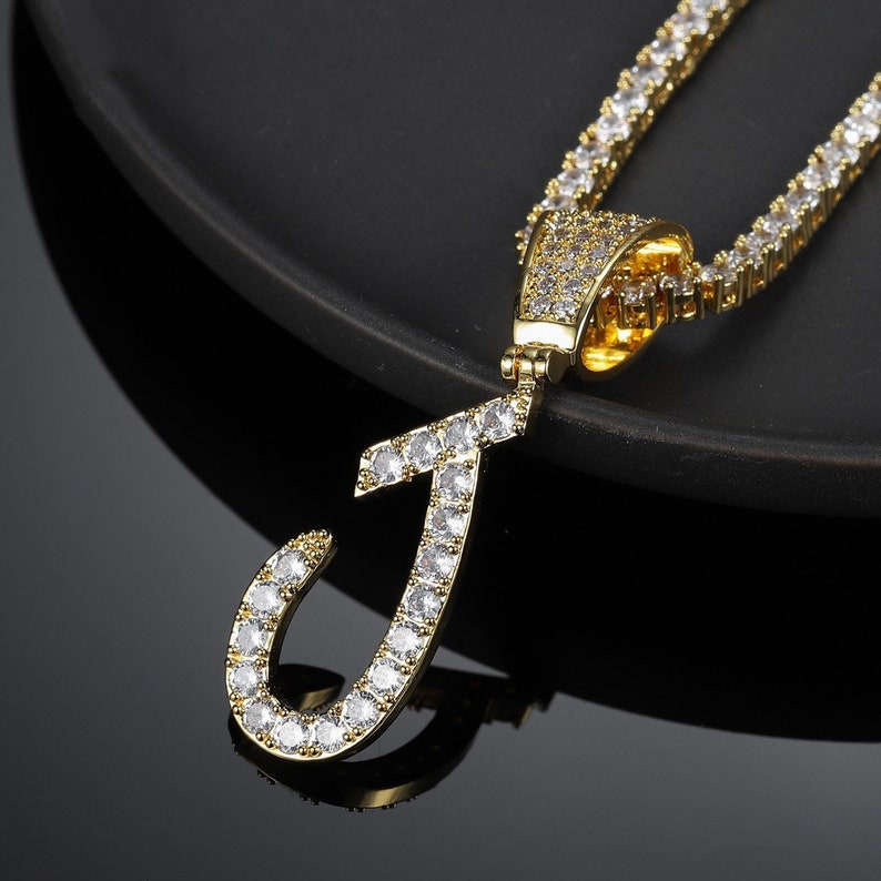 May include: Gold chain necklace with a large, diamond-encrusted letter J pendant.