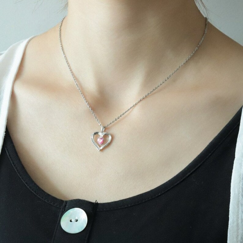 May include: A silver necklace with a delicate heart pendant featuring a pink crystal in the centre.