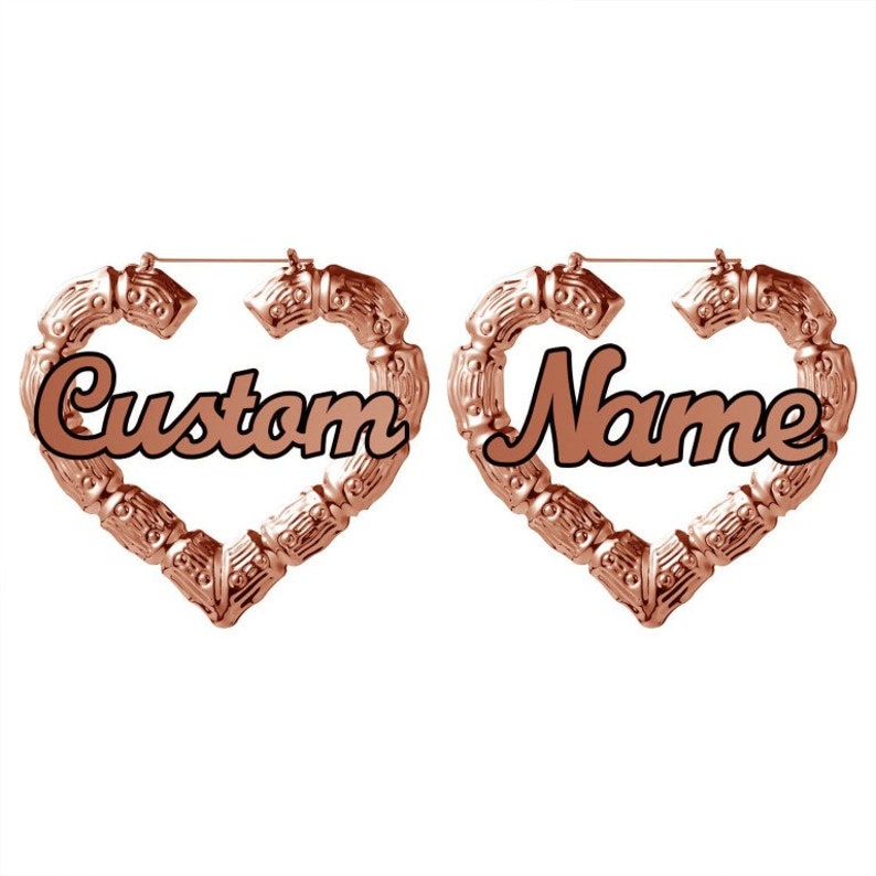May include: A pair of rose gold heart-shaped hoop earrings with the words "Custom" and "Name" written in black cursive lettering.