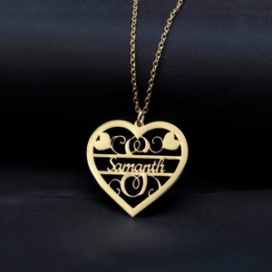 Könnte beinhalten: Eine goldfarbene herzförmige Anhängerkette. Der Anhänger trägt den Namen "Samanth" in einer stilisierten Schriftart, mit dekorativen Elementen und einer filigranen Kette. Die Halskette wird vor einem dunklen Hintergrund gezeigt.