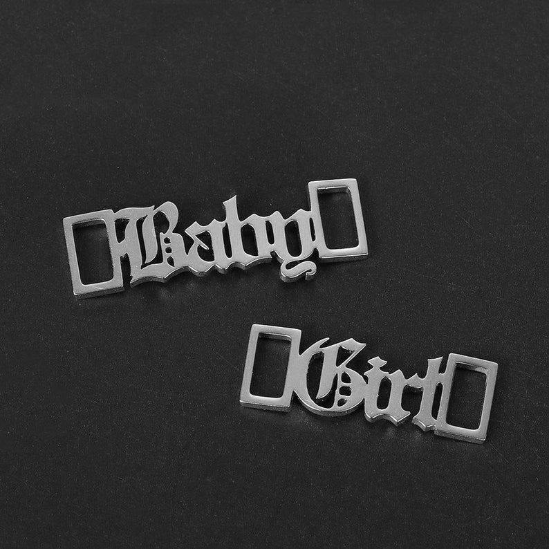 May include: Two silver metal charms with the words "Baby" and "Girl" in a gothic font.