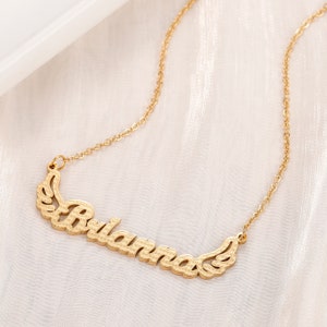 K&ouml;nnte beinhalten: Goldkette mit einer zarten Kette und einem Anh&auml;nger mit dem Namen "Briana" mit Fl&uuml;geln auf beiden Seiten.
