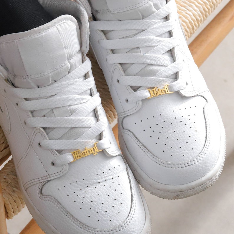 May include: White leather sneakers with gold shoelace charms that say "Badgirl" and "1Girl".