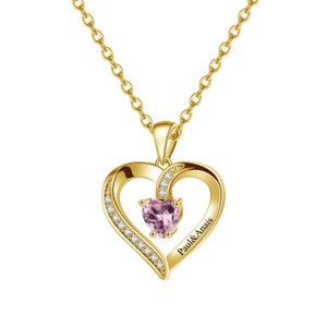 May include: Gold necklace with a heart-shaped pendant featuring a pink gemstone and a smaller heart with the inscription "Paul & Anais".
