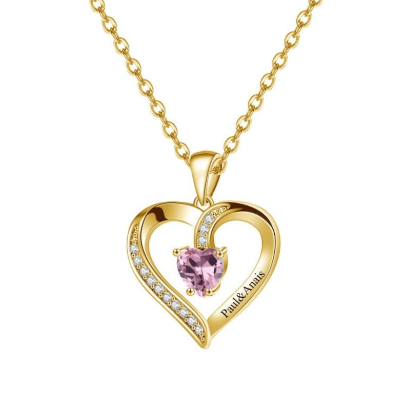 May include: Gold necklace with a heart-shaped pendant featuring a pink gemstone and a smaller heart with the inscription "Paul & Anais".