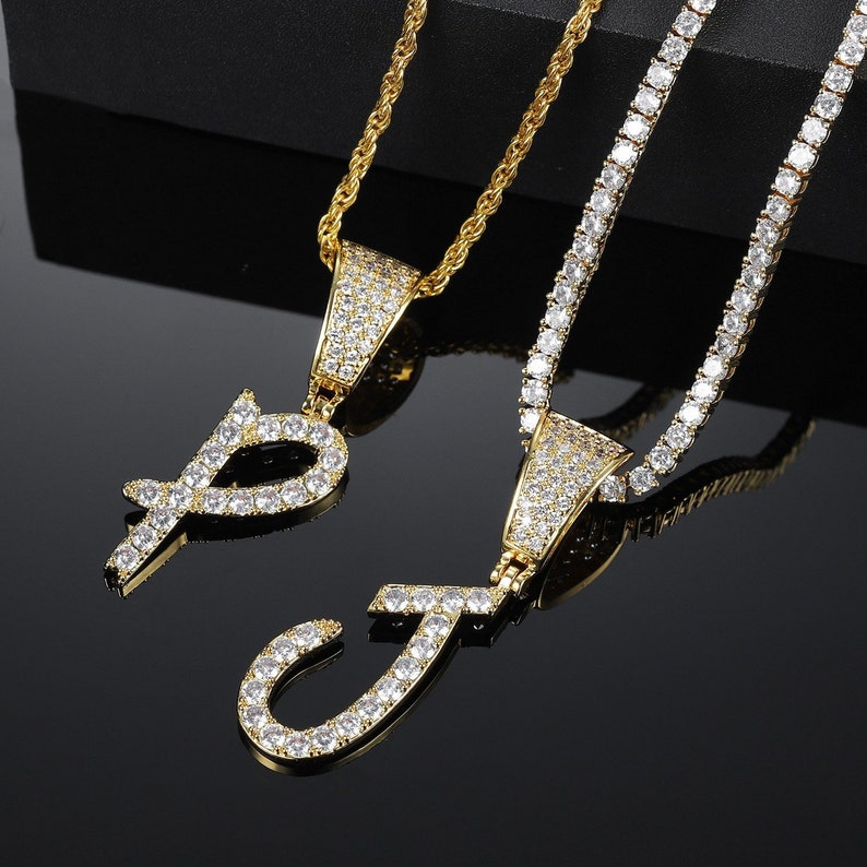 May include: Two gold chains with pendants featuring the letters "P" and "J" encrusted with clear cubic zirconia stones.