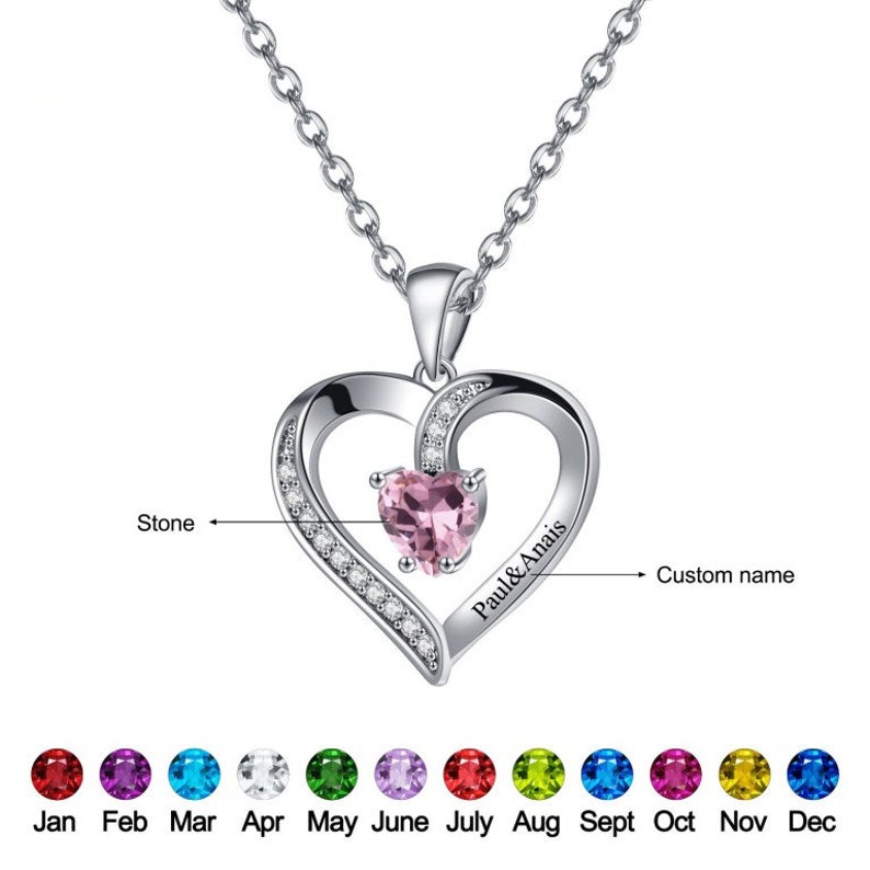 May include: A silver heart necklace with a pink gemstone in the centre. The necklace has a custom name engraved on the side, "Paul & Anais". The pendant is surrounded by small clear gemstones. The necklace comes with a choice of birthstone colours for the centre gemstone.