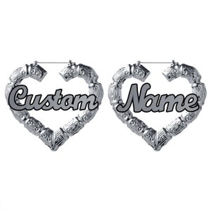 May include: A pair of silver heart-shaped hoop earrings with the words "Custom" and "Name" inscribed on them.