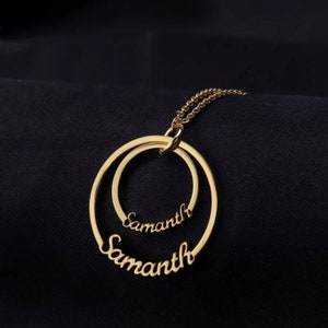 May include: A gold-coloured necklace featuring two interlocking circular pendants. The name "Samanth" is inscribed in a cursive font on each pendant. The necklace hangs on a delicate chain against a dark background.