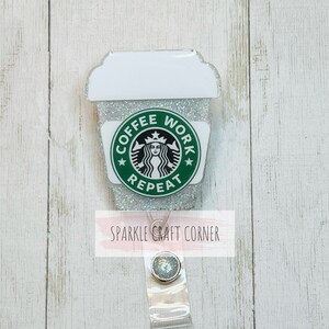 May include: A white coffee cup with a green Starbucks logo and the text "Coffee Work Repeat" on a silver glitter background. The cup is attached to a clear plastic badge holder with a silver glitter button.