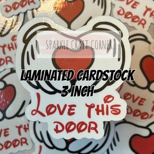 May include: A 7.62 cm laminated cardstock sticker featuring a graphic of two white gloved hands forming a heart shape around a red heart. The text "LOVE THIS DOOR" is printed in red below the hands. The sticker has a white border and glossy finish.