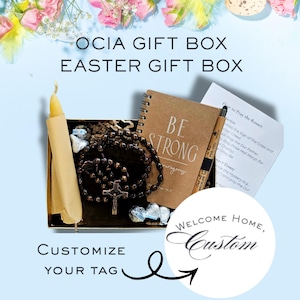 May include: An Easter gift box with a candle, rosary, notebook with "BE STRONG" text, pen, and a card. The box is decorated with flowers and Easter eggs. Text on the image says "OCIA GIFT BOX" and "EASTER GIFT BOX".