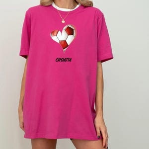 Op de afbeelding: Een roze T-shirt met een afbeelding van een voetbal in de vorm van een hart. De afbeelding bevat ook het woord "KROATI&Euml;".
