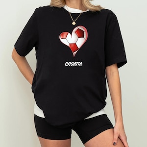 Op de afbeelding: Zwart T-shirt met een rood en wit hartvormig voetbalmotief en het woord "KROATI&Euml;" eronder gedrukt.