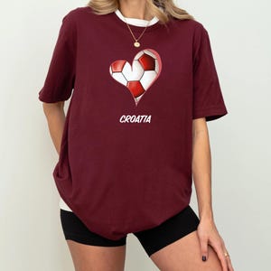 Op de afbeelding: Een maroon t-shirt met een wit hartontwerp met daarin een voetbal. De tekst "CROATIA" is onder het hart gedrukt.