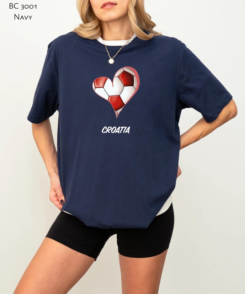 Op de afbeelding: Een marineblauw t-shirt met een rood en wit voetbalontwerp in de vorm van een hart. De tekst "CROATIA" is onder het hart gedrukt.
