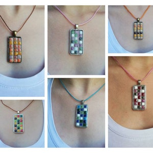 Op de afbeelding: Een verzameling mozaïek hangerkettingen. Elke ketting heeft een rechthoekige hanger met een mozaïektegelontwerp in verschillende kleuren, waaronder oranje, groen, blauw en rood. De hangers hangen aan een koord.