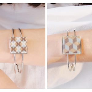 Può includere: Due braccialetti d'argento con inserti quadrati a motivi. Il braccialetto a sinistra ha un motivo geometrico in tonalità di marrone, bianco e oro. Il braccialetto a destra ha un motivo geometrico in tonalità di marrone, bianco e blu.