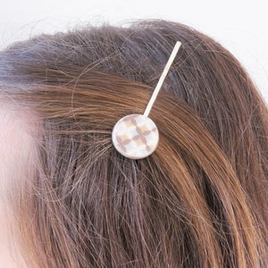Puede incluir: Una pinza para el pelo plateada con un diseño redondo de patrón blanco y marrón.