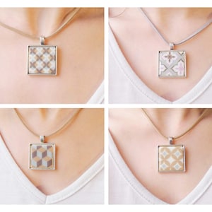 Puede incluir: Cuatro collares con colgantes cuadrados con diferentes patrones geométricos. Cada colgante tiene un marco plateado y cuelga de un cordón fino. Los patrones incluyen un diseño a cuadros, floral, cubo y circular, en tonos neutros.