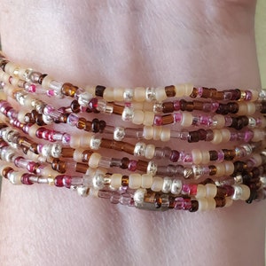May include: A multi-strand bracelet made of small, colorful beads. The bracelet is made of beige, brown, pink, and silver beads.