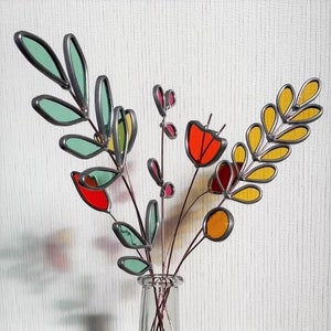May include: A glass vase with a bouquet of colorful stained glass flowers. The flowers are made of different colors of glass, including red, orange, yellow, and green. The vase is clear glass and has a round shape.