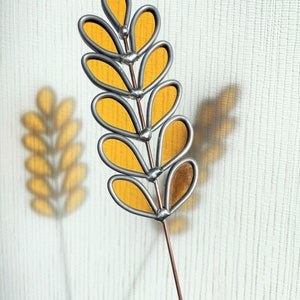 May include: A stained glass floral stem with yellow glass leaves and a silver wire frame. The stem is attached to a copper wire.